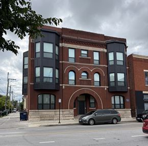 Chicago apartment for rent - A grey van is parked in front of a red brick building with a black extension.