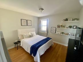 Chicago apartment for rent - A bedroom with a bed, a window, and a shelf with plants and pictures.