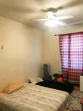 Chicago apartment for rent - A bedroom with a bed, a ceiling fan, and a window with curtains.