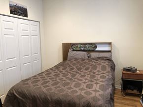 Chicago apartment for rent - A bed with a brown patterned comforter sits in a room with a white door and a poster on the wall.
