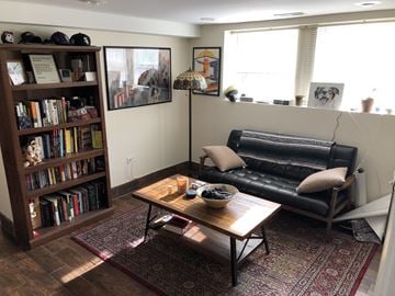 Chicago apartment for rent - A living room with a black leather couch, a wooden bookshelf filled with books, a coffee table with a bowl of fruit on it, and a rug on the floor.