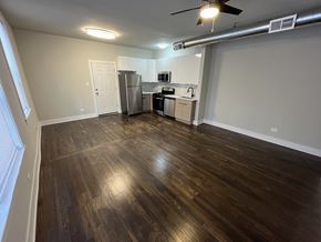 Chicago apartment for rent - A room with wooden flooring and a kitchen area in the background.