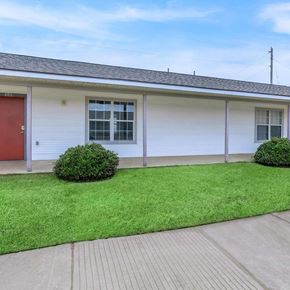 Shreveport apartment for rent - A small white house with a red door and a green lawn in front.