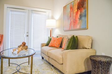 Gonzales apartment for rent - A living room with a beige couch, a glass table, a lamp, and a painting on the wall.