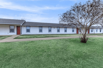 Shreveport apartment for rent - A white building with a red door and a tree in front.