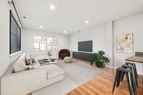 Philadelphia apartment for rent - A living room with a white couch, a brown armchair, a grey rug, a wooden floor, a TV, a plant, and pictures on the wall.