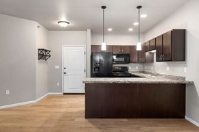 Mandan apartment for rent - A kitchen with a black refrigerator and brown cabinets.