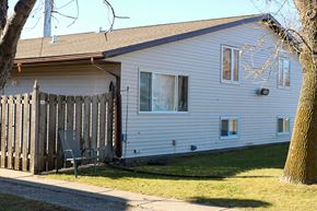 West Fargo triplex for rent - A white house with a brown roof and a grey chair in front of it.