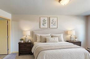 West Fargo apartment for rent - A bedroom with a large bed, two nightstands with lamps, and two framed pictures on the wall.