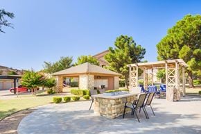 Lubbock apartment for rent - A patio with a table and chairs is surrounded by a stone wall and trees.