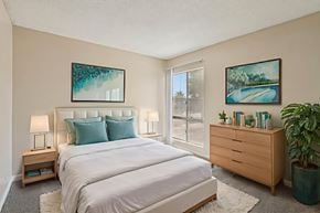 Las Vegas apartment for rent - A bedroom with a large bed, a nightstand with a lamp, a dresser with a plant, and two framed pictures on the wall.