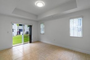 Hialeah apartment for rent - A spacious room with tiled flooring and a sliding glass door leading to a backyard.