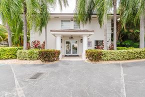 Miami apartment for rent - A white building with a black door and windows surrounded by greenery.