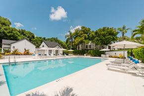 Coconut Creek apartment for rent - A large swimming pool surrounded by lounge chairs and umbrellas with a house in the background.