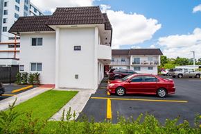 Miami apartment for rent - A red car is parked in a parking lot in front of a white building with a black roof.
