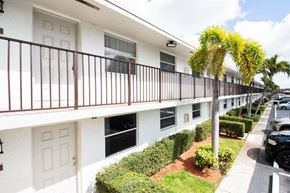 Hialeah apartment for rent - A row of white apartment buildings with brown railings and a tree in front.