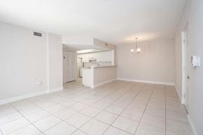Miami apartment for rent - A white tiled kitchen and living room with a white cabinet and a white fridge.