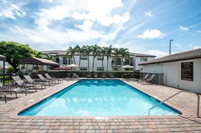 Miami apartment for rent - a swimming pool with chairs and a building in the background