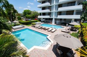 South Miami apartment for rent - A large swimming pool surrounded by lounge chairs and umbrellas in front of a white apartment building.