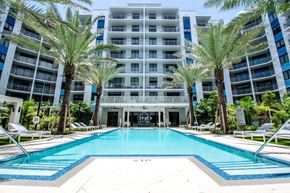 Miami apartment for rent - a large swimming pool in front of an apartment building with palm trees