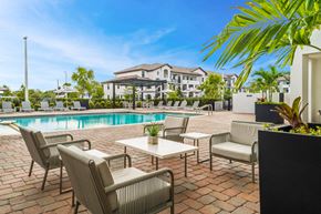 Hialeah apartment for rent - a swimming pool with chairs and tables and a building in the background