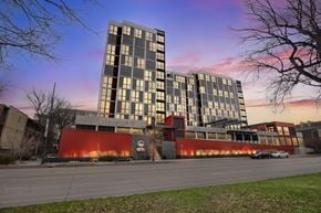Denver apartment for rent - A modern building with a red and grey facade stands in front of a tree.