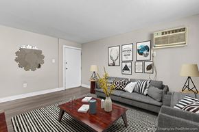 Denver apartment for rent - A living room with a grey couch, a coffee table, and a wall with pictures and an air conditioner unit.