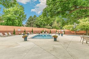 Lakewood apartment for rent - A pool surrounded by a concrete patio and trees.