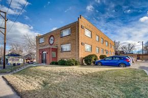 Denver apartment for rent - A blue car is parked in front of a brick building with a red circle on the front.