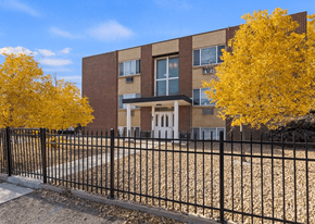 Commerce City apartment for rent - A brick building with a black fence and yellow trees in front.