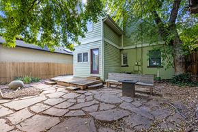 Denver apartment for rent - A house with a green siding and a brown door is surrounded by a stone patio and trees.