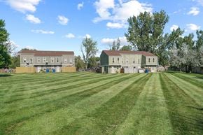 Lafayette triplex for rent - Two buildings sit on a green field with trees in the background.
