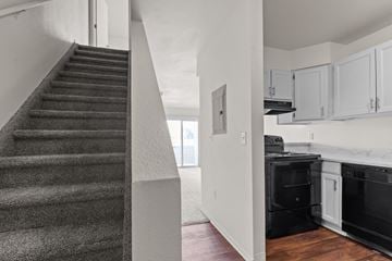 Longmont apartment for rent - A staircase leads to a kitchen area with white cabinets and black appliances.