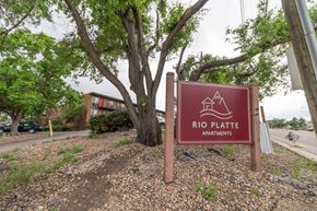 Denver apartment for rent - A sign for Rio Platte Apartments is displayed in front of a tree.