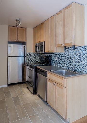 Boulder triplex for rent - A kitchen with wooden cabinets and a black and white tiled backsplash.