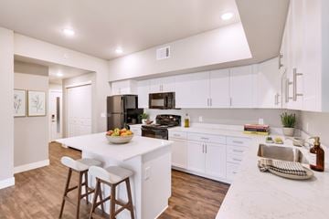 Fort Collins apartment for rent - A kitchen with white cabinets and a white island with a bowl of fruit on it.