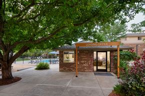 Longmont apartment for rent - A leasing office is surrounded by greenery and has a pool in the background.