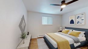 Arvada apartment for rent - A bedroom with a bed, a plant, and a mirror.