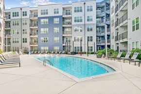 Charlotte apartment for rent - A swimming pool is surrounded by lounge chairs in front of apartment buildings.