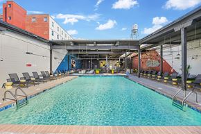 Winston-Salem apartment for rent - A large indoor swimming pool with a blue tiled edge and black lounge chairs on the side.