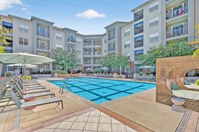 Atlanta apartment for rent - A large swimming pool surrounded by lounge chairs and umbrellas in front of apartment buildings.