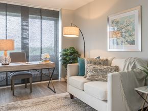 Halifax apartment for rent - A living room with a white couch, a desk with a chair, a floor lamp, and a framed picture on the wall.