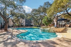 San Antonio apartment for rent - A swimming pool surrounded by trees and a patio area.