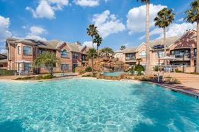 Houston apartment for rent - West Houston, TX, Apartments Near Shell Houston - San Montego - Resort-Style Pool With Rock Waterfall, Palm Trees, Lounge Seating, And Brick Apartment Buildings Under Blue Sky.