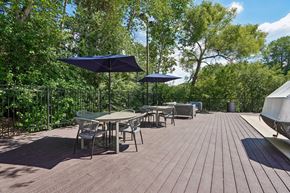 Eden Prairie apartment for rent - A wooden deck with chairs and tables is surrounded by green trees.