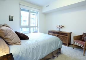 Mercer Island apartment for rent - Mercer Island, WA Apartments with In-Unit Washer and Dryer - 77 Central - A bright, modern bedroom with a large window, a light blue bedspread, and a rustic wooden dresser.