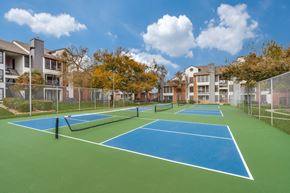 Austin apartment for rent - A tennis court surrounded by a fence and buildings.