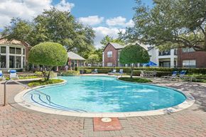 Plano apartment for rent - A large swimming pool surrounded by a brick patio and trees.