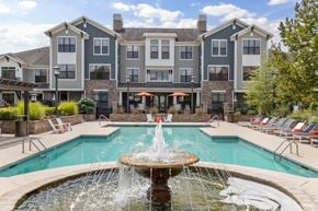 Charlotte apartment for rent - Dog-Friendly Apartments in Charlotte, NC - The Apartments at Blakeney - Swimming Pool with a Water Fountain, Sun Loungers, Lounge Chairs, Small Tables, Umbrellas, and Lush Landscaping.