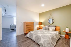 Seattle apartment for rent - Studio Apartments In Green Lake, Seattle, WA - Circa Green Lake - Spacious Bedroom With Hardwood Floor, Bed, Round Mirror, Nightstand with Lamp, Round Side Table, Dresser, and View of Living Room.